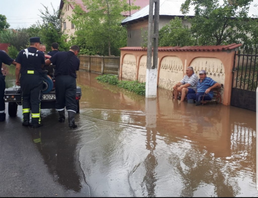 Fotografia zilei: doi localnici stau pe bancă în timp ce pompierii scot apa din comună