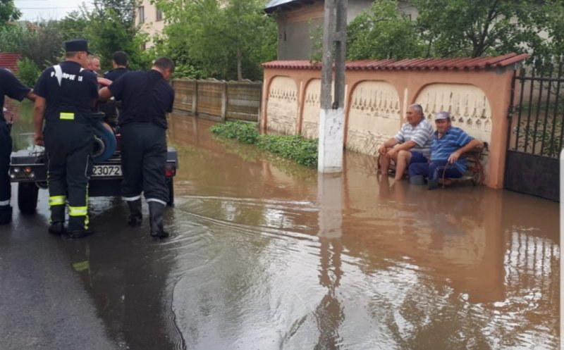 Fotografia zilei: doi localnici stau pe bancă în timp ce pompierii scot apa din comună